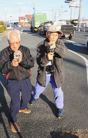 当時の聖火リレーコースとなった道路の脇で８ミリカメラを構える鈴木芳朗さん（右）＝湖西市新居町で