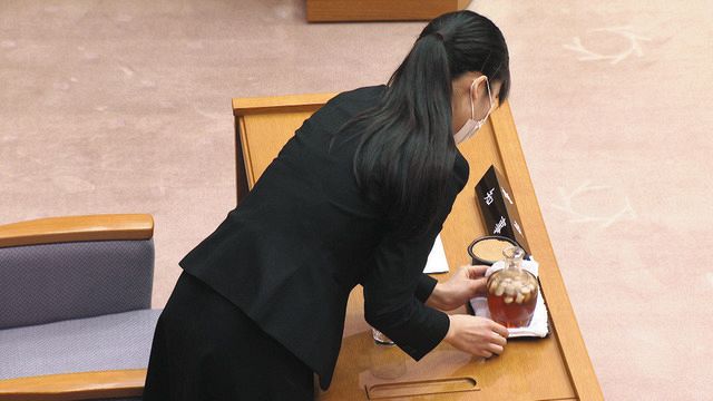 映画「裸のムラ」の一場面。石川県議会の議場で女性職員が知事席の水差しの水滴を拭き取っている（©石川テレビ放送）