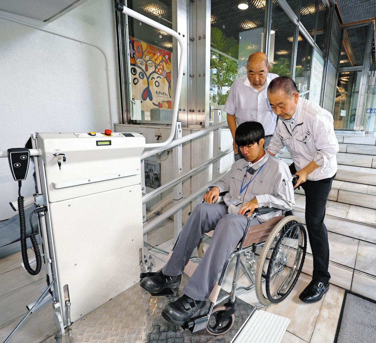 正面階段に設置された車いす用リフトの運用テストを行う関係者たち＝東京都千代田区の中日新聞東京本社で（平野皓士朗撮影）