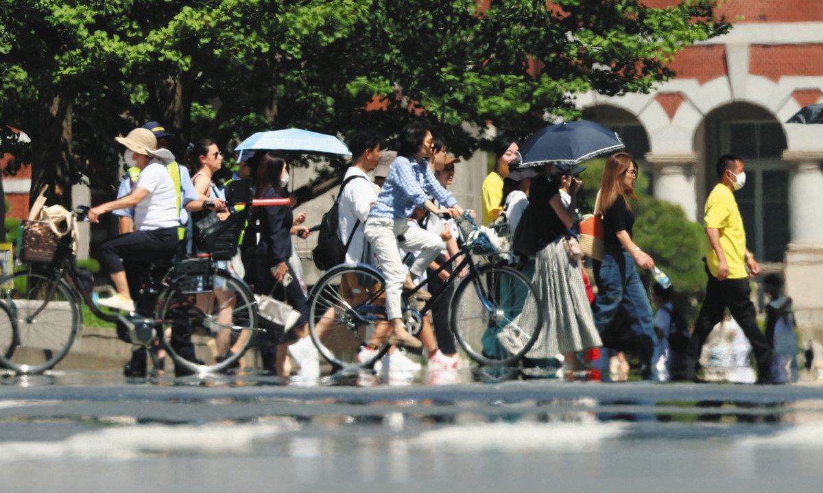 厳しい日差しが照りつけ「逃げ水」が現れる中、日傘を差して歩く人たち＝7月2日、千代田区で