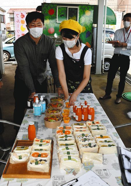 手作りのサンドイッチなどをテーブルに並べる加納慶太さん（左）と智恵さん（中）。後方はキッチンカー＝船橋市で
