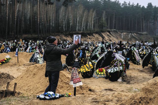 21日、ウクライナの首都キーウ近郊イルピンの墓地で、ロシア軍の占拠中に亡くなった父の遺影に触れる女性＝AP
