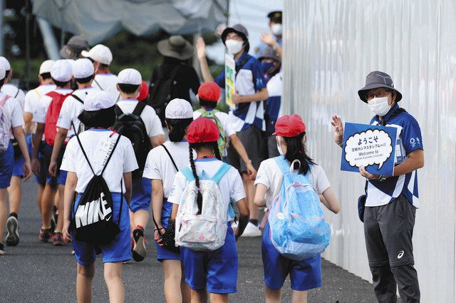 子どもらに手を振りながらスタジアムまで誘導する都市ボランティア（右） 