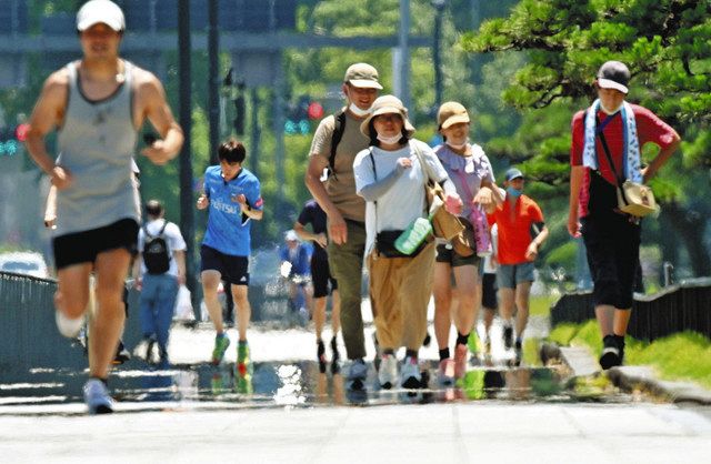 都内で今年初の猛暑日となり、かげろうや逃げ水が現れた歩道を行きかう人たち＝東京都千代田区で