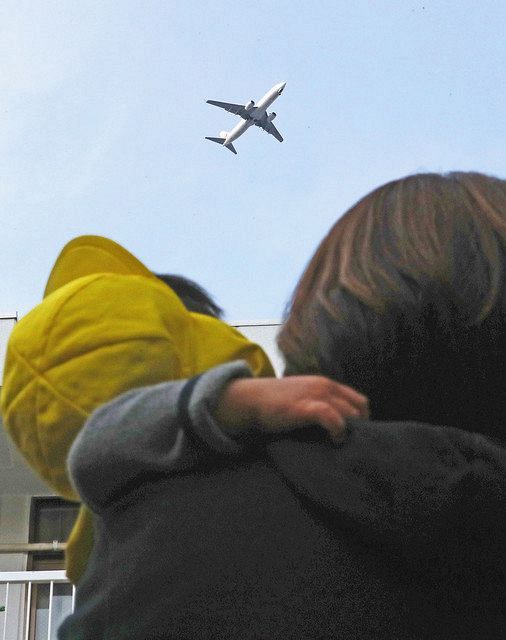 羽田空港への新ルートを低空飛行する飛行機と、それを見つめる保育士と園児＝４月、東京都港区で