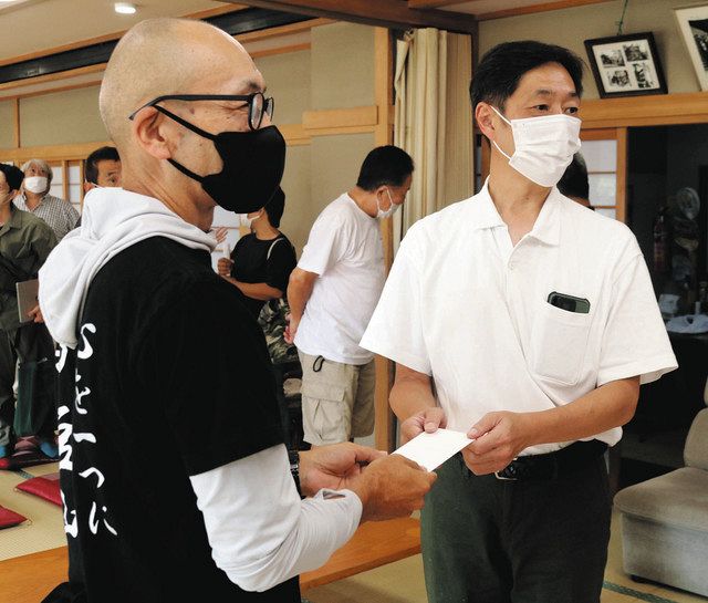 ボランティア団体の男性（左）から支援金を受け取る被害者の会の瀬下雄史さん＝熱海市伊豆山で 