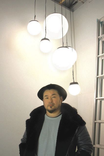 電球を月に見立てた作品の前に立つ主宰者の渡辺篤さん＝横浜市西区で