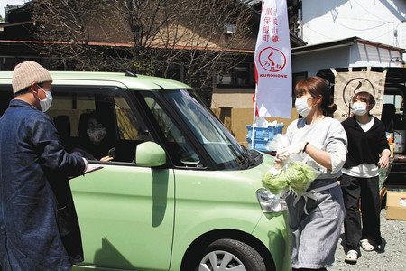 桐生市にオープンした「ドライブスルー八百屋」で注文を取る岩崎大輔さん（左）。開店２時間弱で完売し、大盛況だった