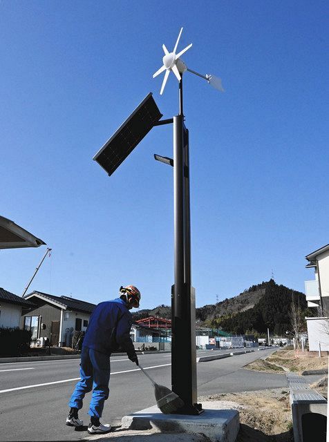 街灯の新設を終え、掃除する男性。街灯には太陽光発電パネルや風車が付き、自家発電した電気で道を照らす＝福島県大熊町で