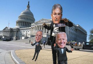 米ワシントンの議事堂前で２０日、バイデン大統領（右）の大型歳出法案に反対する民主党上院議員らにふんしてやゆする環境活動家＝ＡＰ
