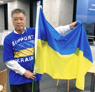 ウクライナ国旗を手に「『命のビザ』とともに募金も人道の一つ。多くの人に知ってほしい」と話す稲葉教授＝名古屋市東区の名城大で