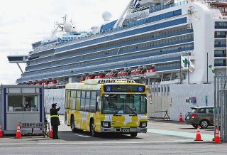 クルーズ船「ダイヤモンド・プリンセス」（後方）から下船した人たちを乗せ、出発するバス＝２月、横浜市鶴見区の大黒ふ頭で