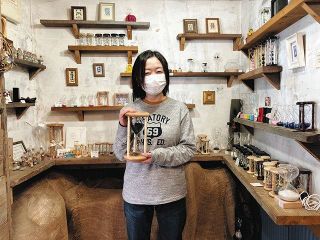 店内で、オーナーの和田朱美さん。手に持っているのは、１時間計れる大型の砂鉄砂時計
