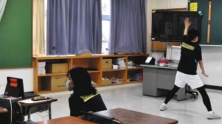 校内で、撮影のために体を動かす教員（右）と、家庭にいる子どもにタブレットを通じて声を掛ける教員

