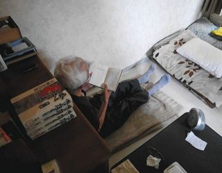 料金未払いのため電気を止められた小さな部屋で、読書をして過ごす男性＝杉並区で
