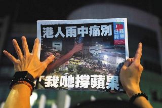 ２４日付の香港紙、蘋果日報を掲げる人＝ロイター・共同